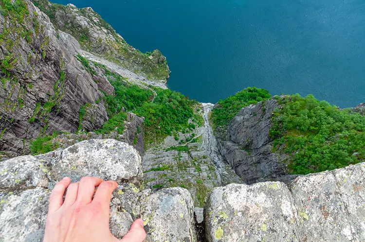 Hand resting on the Preikestolen cliff edge above the drop to Lysefjord